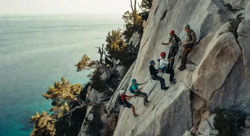 Trekkers rappelling down a limestone cliff on the Selvaggio Blu with the turquoise Gulf of Orosei visible below on a 7-day sardinia multi day trek